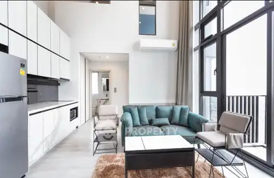 Modern living room with open kitchen, featuring sleek design and large windows for natural light.