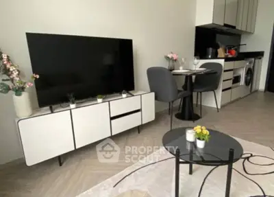 Modern open-plan living space with sleek furnishings, including a large TV, dining area, and a fully equipped kitchen with washing machine.