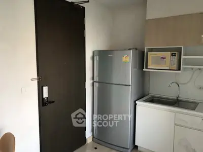Compact kitchen with fridge, microwave, and sink in modern apartment.