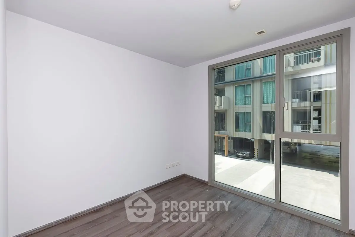 Spacious empty room with large window and modern flooring in urban apartment