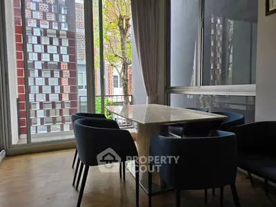 Modern dining area with sleek table and chairs, large windows offering natural light and urban view.