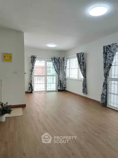 Spacious living room with wooden flooring and large windows, perfect for natural light.