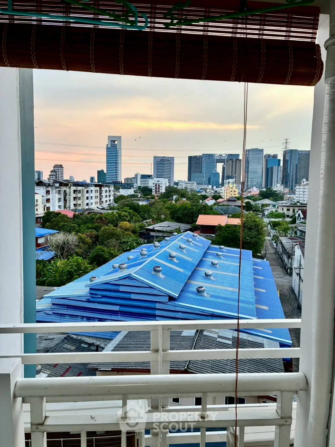Stunning cityscape view from a high-rise balcony overlooking urban skyline and rooftops at sunset.