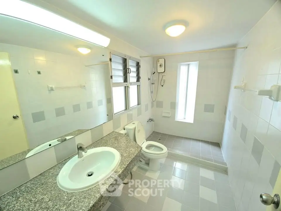 Spacious bathroom with modern fixtures and large mirror in bright apartment.