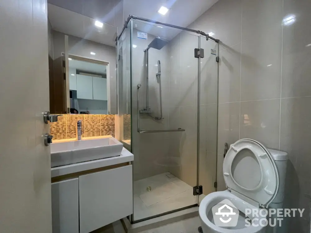 Modern bathroom with glass shower and sleek vanity in contemporary apartment.