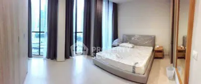 Spacious bedroom with large windows and city view, featuring a modern bed and elegant decor.