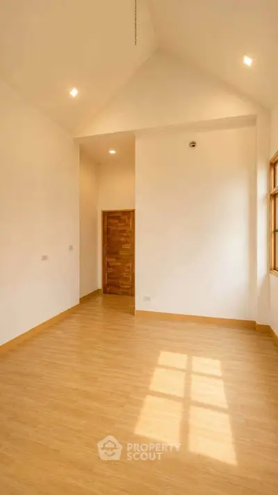 Spacious empty room with wooden flooring and high ceiling, perfect for customization.