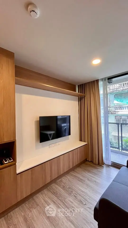 Modern living room with sleek wooden cabinetry and mounted TV, featuring large window for natural light.