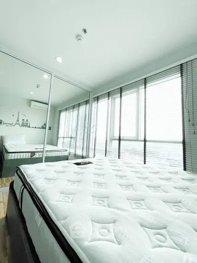Modern bedroom with mirrored closet and large windows offering city views.