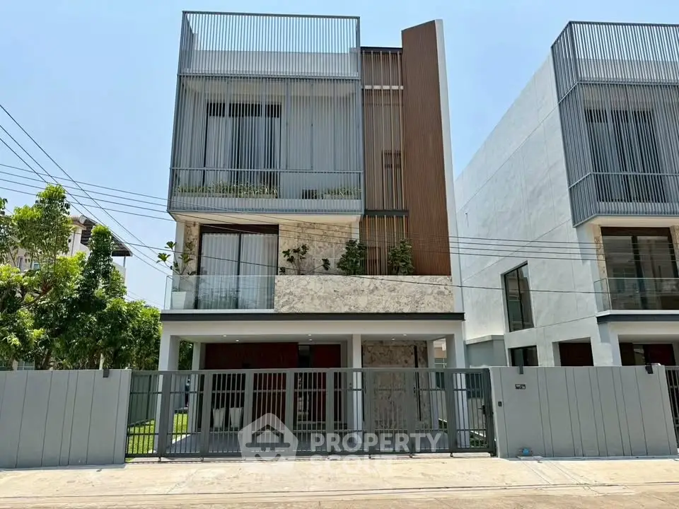 Modern three-story house with sleek design and gated entrance, featuring large windows and contemporary facade.