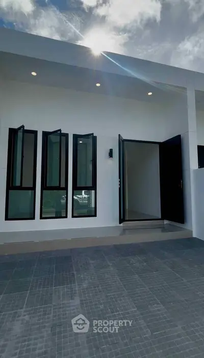 Modern minimalist building exterior with sleek black-framed windows and open door under a bright sky.