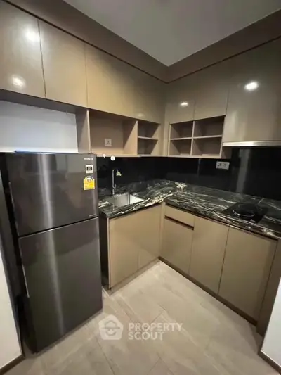 Modern kitchen with sleek cabinetry and stainless steel fridge in a compact layout.