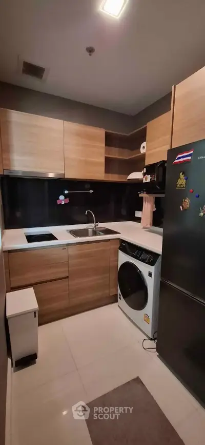 Modern kitchen with wooden cabinets, sleek appliances, and washing machine in compact layout.