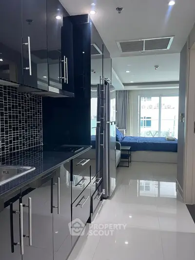 Sleek modern kitchen with glossy cabinets and open layout leading to a cozy bedroom.