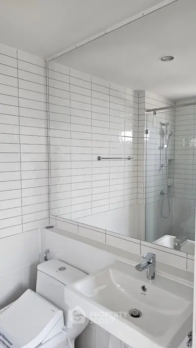 Modern bathroom with sleek white tiles and glass shower enclosure.