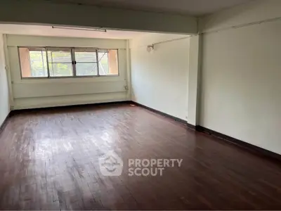 Spacious empty room with wooden flooring and large window, ideal for customization.