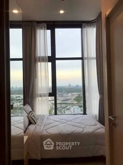 Cozy bedroom with stunning city view through large windows, perfect for urban living.