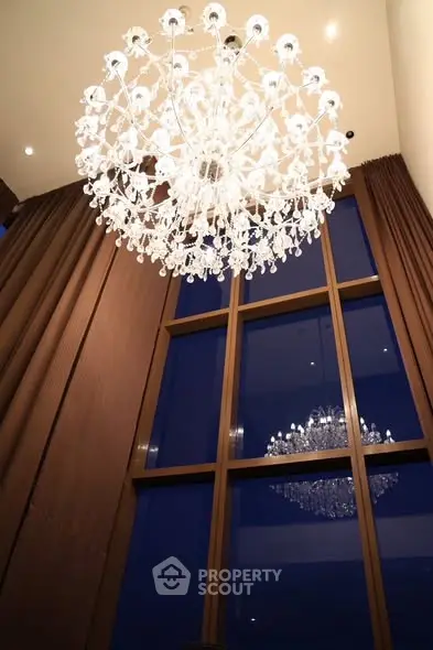 Luxurious high-ceiling living room with elegant chandelier and floor-to-ceiling windows.