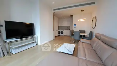 Modern living room with sleek furniture and open kitchen layout, featuring a large TV and elegant lighting.