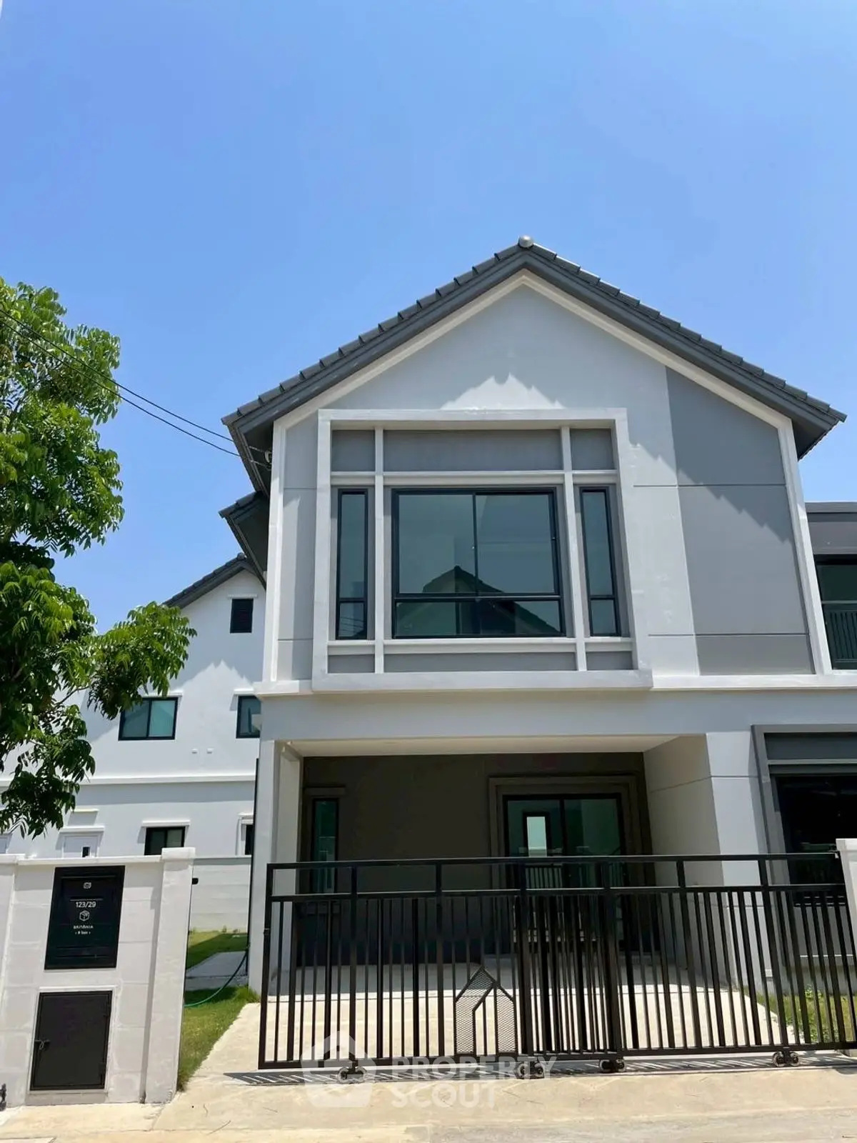 Modern two-story house with sleek design and gated entrance under a clear blue sky.
