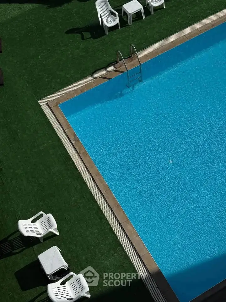 Luxurious outdoor swimming pool with stylish seating on lush green artificial grass, perfect for relaxation.