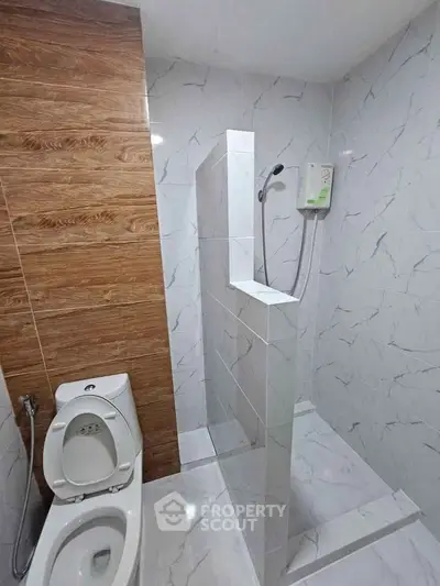 Modern bathroom with marble tiles and wooden accent wall, featuring a sleek shower area and toilet.