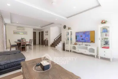 Spacious living room with modern decor and open layout, featuring a large TV and elegant furniture.