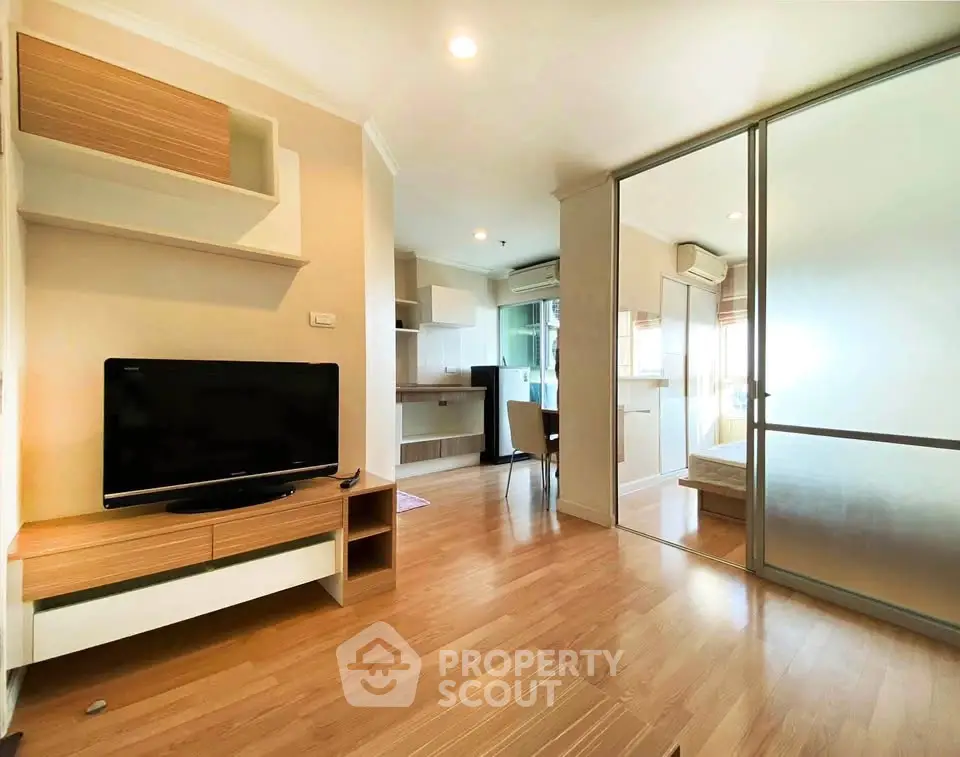 Modern living room with wooden flooring and sliding glass doors leading to a bedroom.