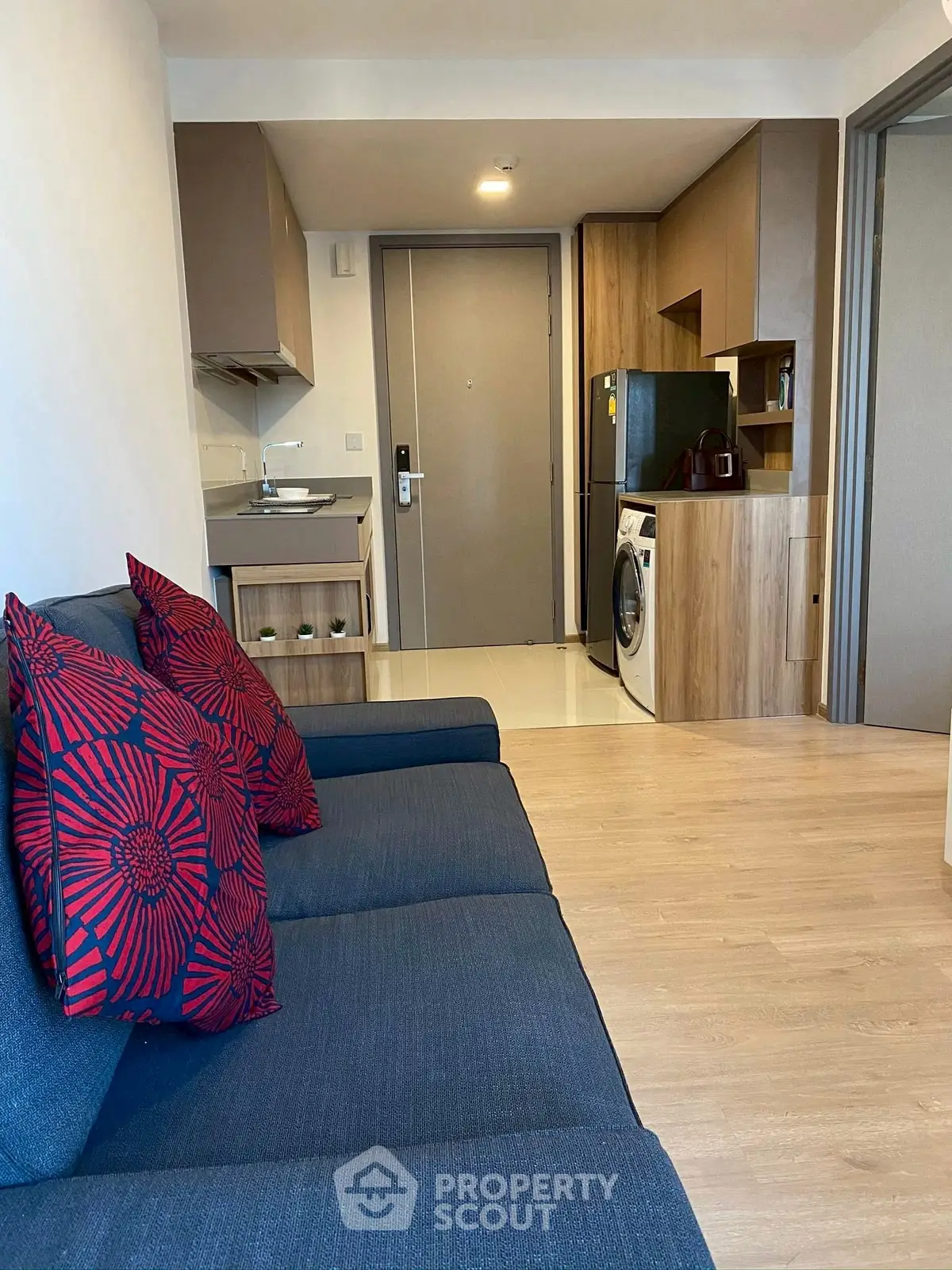 Modern apartment interior with cozy living room and compact kitchen featuring washing machine and fridge.