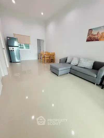 Spacious living room with modern sofa and dining area, featuring sleek tile flooring and natural light.