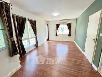 Spacious empty room with wooden flooring and large windows, perfect for customization.