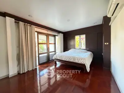 Spacious bedroom with wooden flooring and large windows in a modern home.