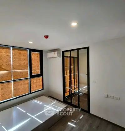 Modern bedroom with large windows and mirrored closet doors, featuring sleek flooring and air conditioning.