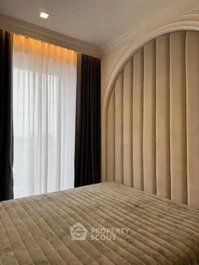 Luxurious bedroom with elegant padded wall and floor-to-ceiling window drapes.