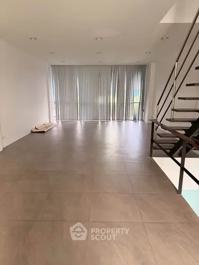 Spacious modern living room with large windows and sleek staircase, perfect for contemporary living.