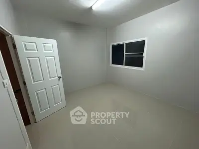 Minimalist empty room with tiled floor and white walls, featuring a window and open door.