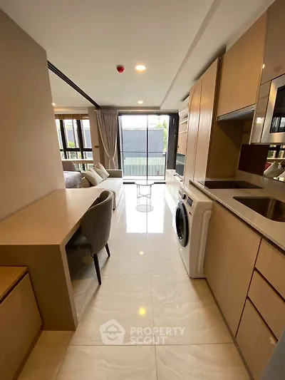 Modern open-plan living room with kitchen and washing machine, featuring sleek design and natural light.