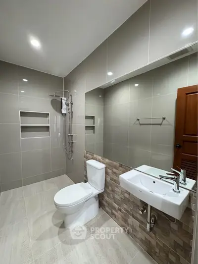 Modern bathroom with sleek fixtures and neutral tiles, featuring a shower and stylish sink.
