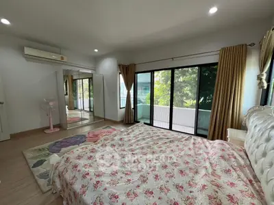 Spacious bedroom with large windows and mirrored closet, featuring elegant floral bedding.