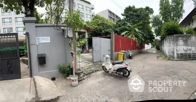 Charming residential entrance with scooter parking, lush greenery, and modern building backdrop.