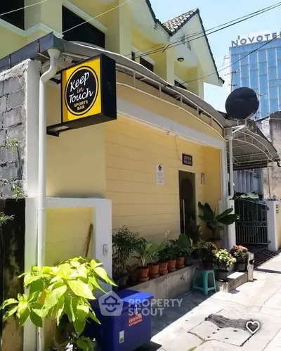 Charming yellow exterior of a small sports bar with lush plants and cozy entrance.