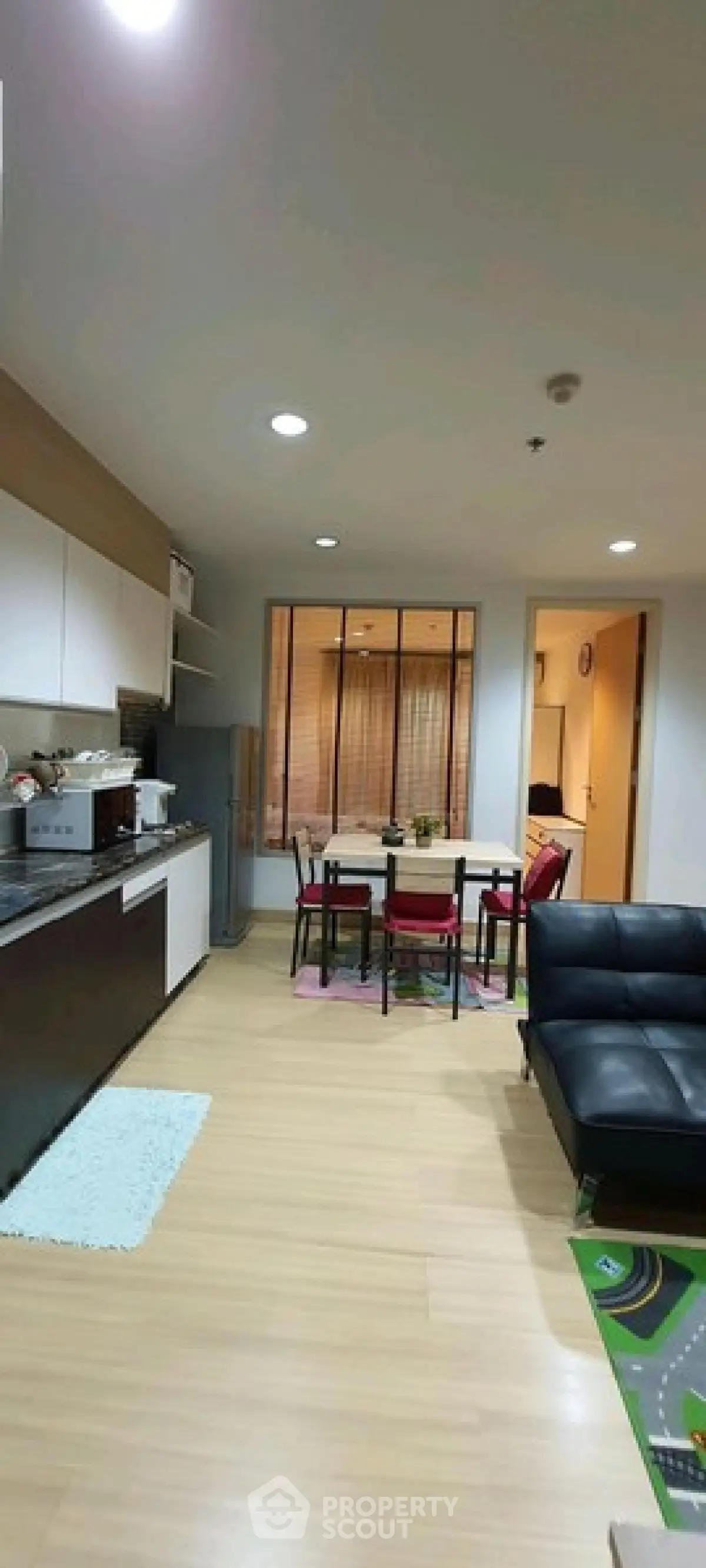 Modern open-layout living room with kitchen, dining area, and sleek black sofa.