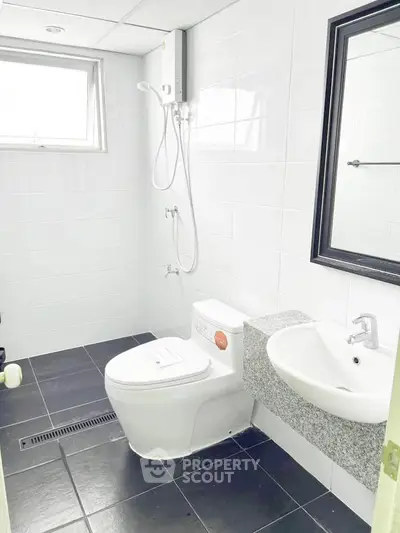 Modern bathroom with sleek black tiles and white fixtures, featuring a shower and a large mirror.