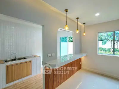 Modern kitchen with open layout and stylish lighting, featuring a sleek countertop and large window with garden view.