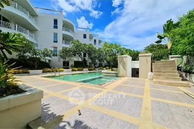 Luxurious apartment complex with stunning pool and lush greenery under a bright blue sky.
