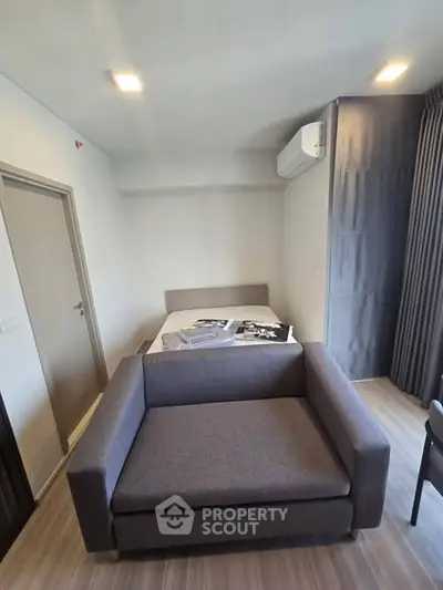 Modern studio apartment with cozy bed and stylish sofa, featuring sleek air conditioning and elegant curtains.