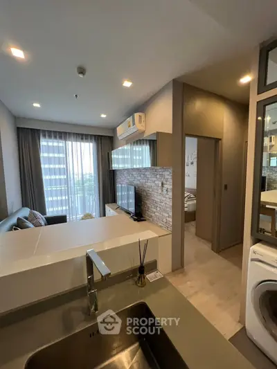Modern open-plan living room with kitchen and washing machine, featuring stylish decor and natural light.