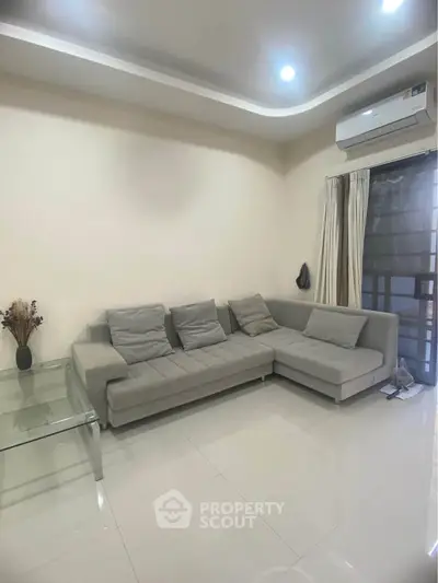 Modern living room with sleek gray sofa and glass table, featuring air conditioning and elegant lighting.