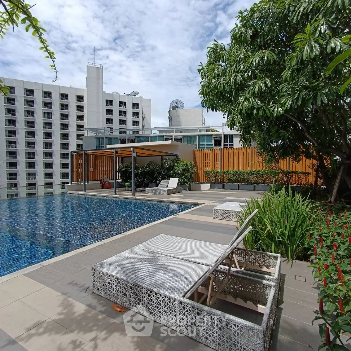 Luxurious rooftop pool area with modern lounge chairs and lush greenery, perfect for relaxation and leisure.