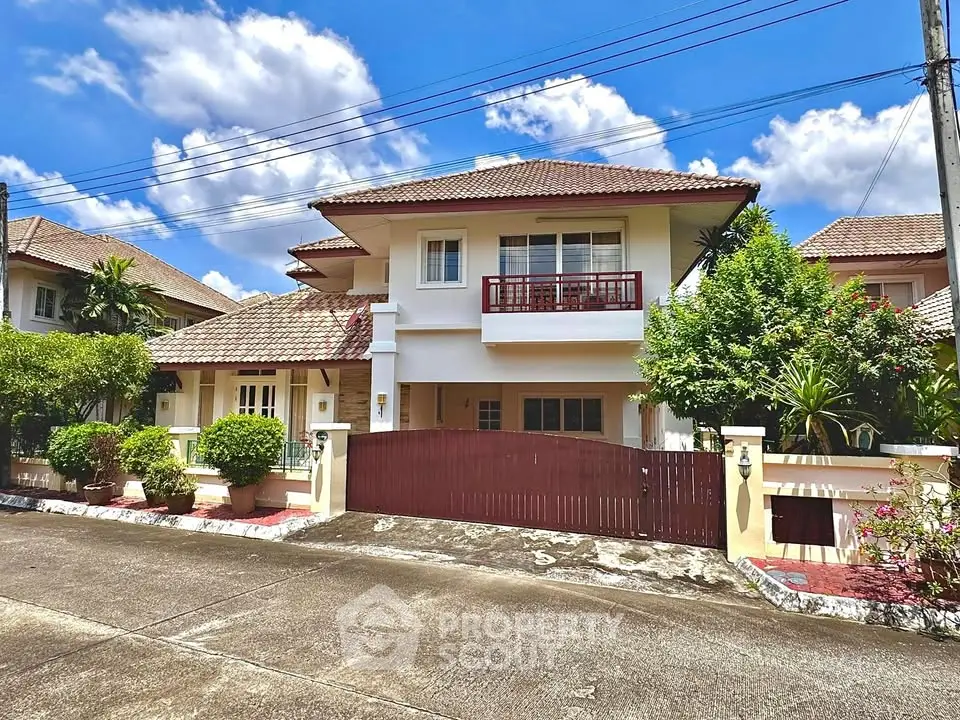 Charming two-story house with red accents and lush greenery under a bright blue sky.